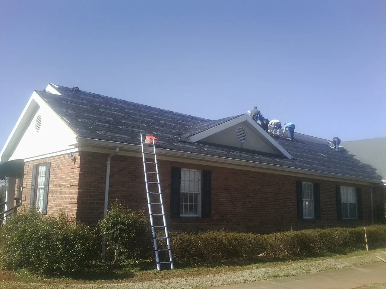 Crew tearing shingles off a brick ranch roof with a ladder set — Metal Roof Repair work by our crew in Saratoga
