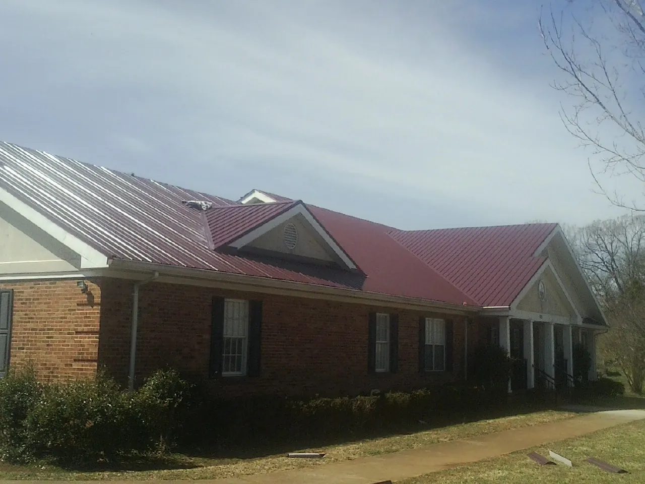 Red metal roof with gabled entries on a long brick building, from a Hail Damage Roof Repair job in Saratoga